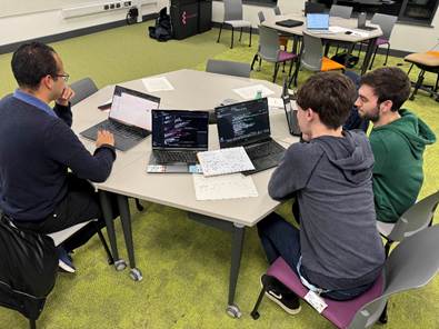 A group of people sitting around a table with laptops