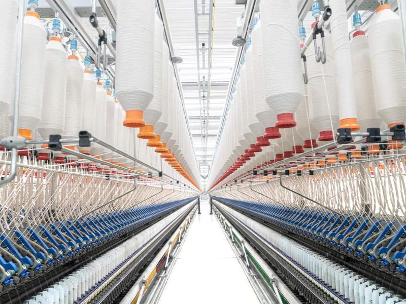 The image depicts a textile factory or mill, specifically showcasing the spinning process where raw fibers are transformed into yarn. 