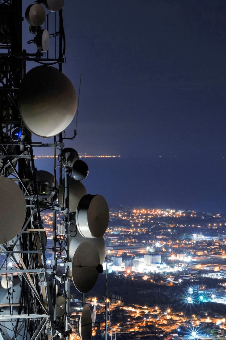 A mast with satellites against the backdrop of the city at night