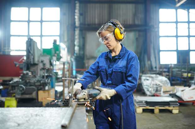 A woman in a blue jumpsuit and yellow headphones, in a workshop electropolishing metal materials