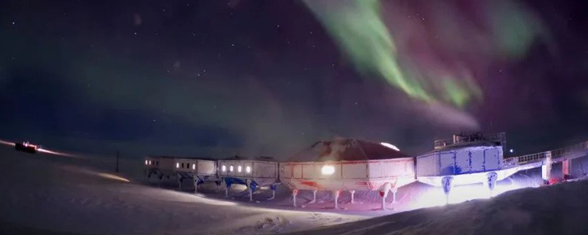 A modular polar research station at night under a vibrant green and purple aurora, illustrating data infrastructure in harsh climates.