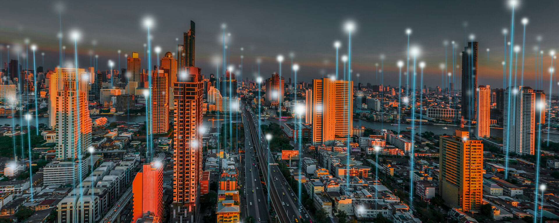 An overlooking shot of a city at night, with beams of light projecting from buildings to represent connectivity and technology in smart cities.