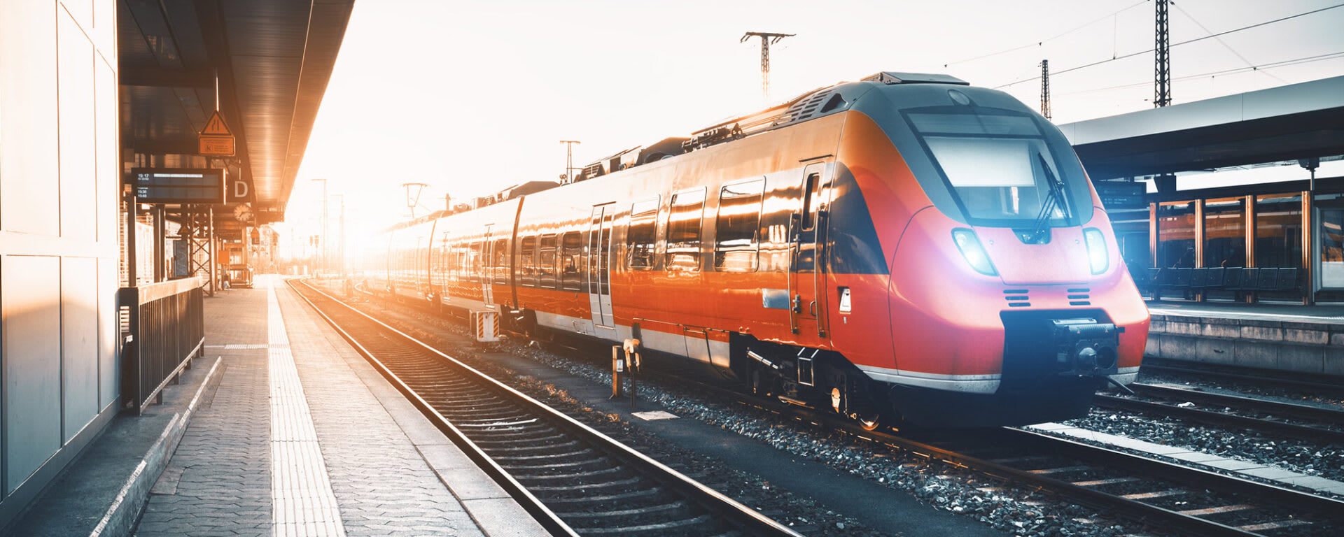 An orange high speed train passing by a train station