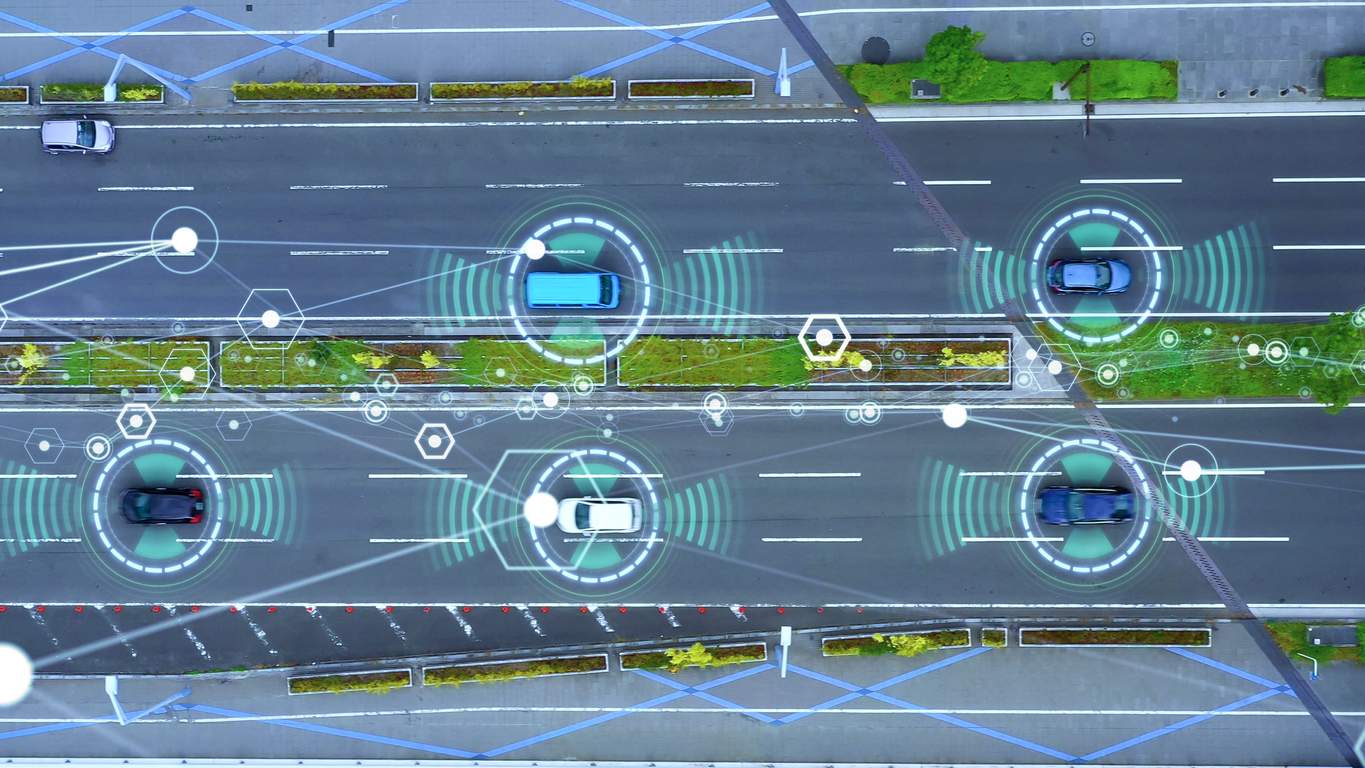 Aerial view of cars on a city road with glowing green circles and white lines representing a connected digital network for smart traffic management.