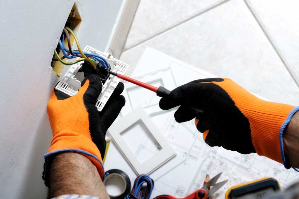 Un elettricista che lavora in sicurezza su interruttori e prese di un impianto elettrico residenziale.
