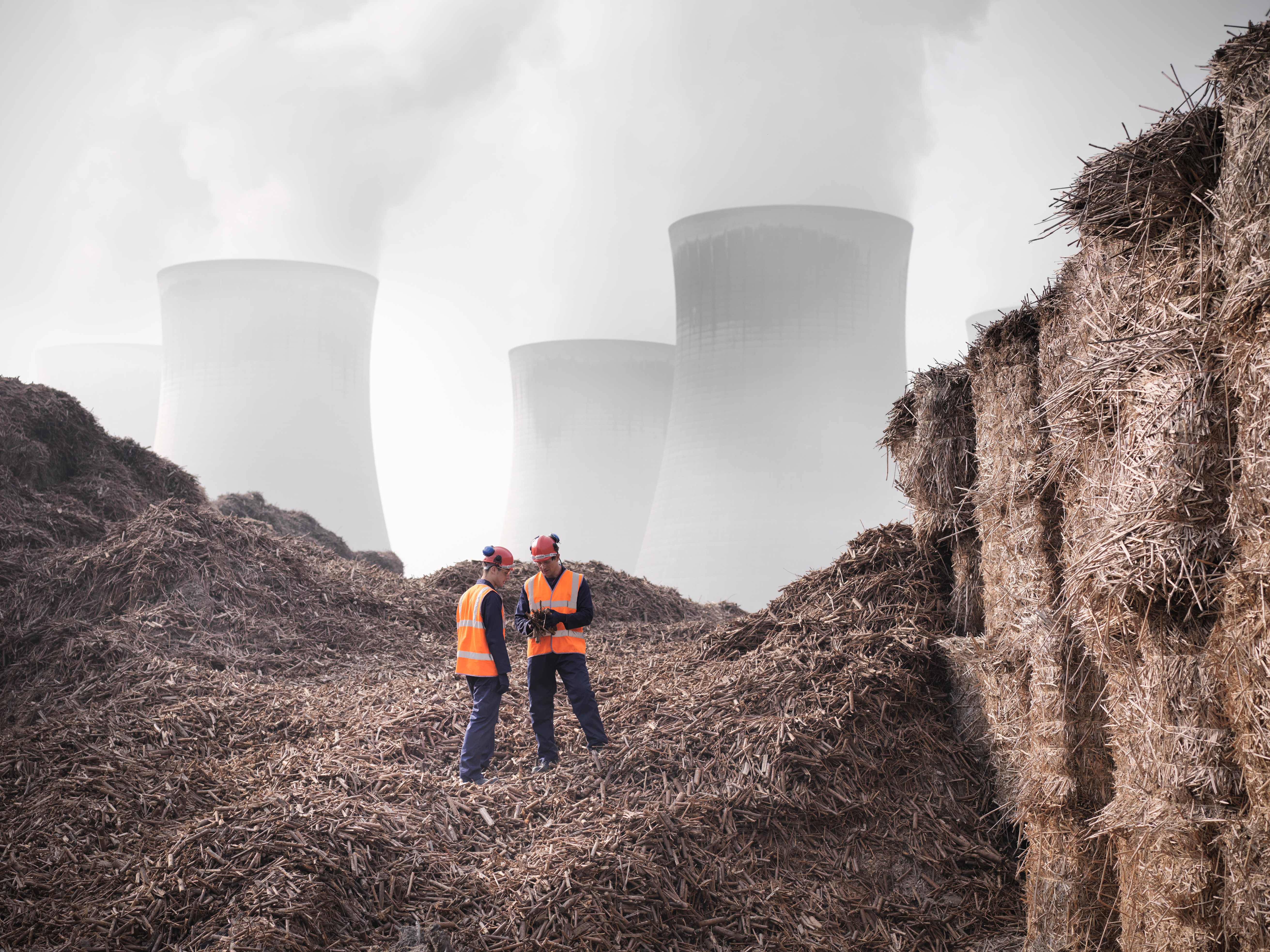 Two engineers standing on a hill, overlooking an operational fossil fuel power plant in the distance.