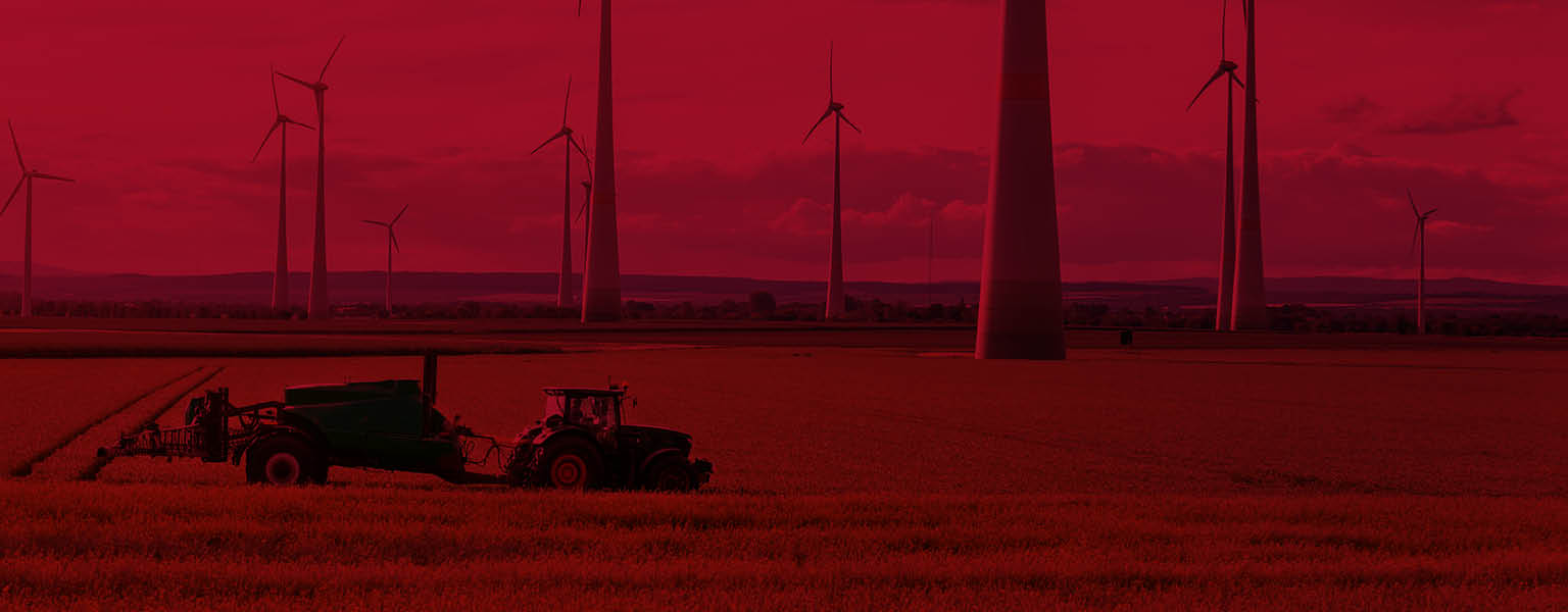 A distant shot of a tractor in a field surrounded by wind turbines