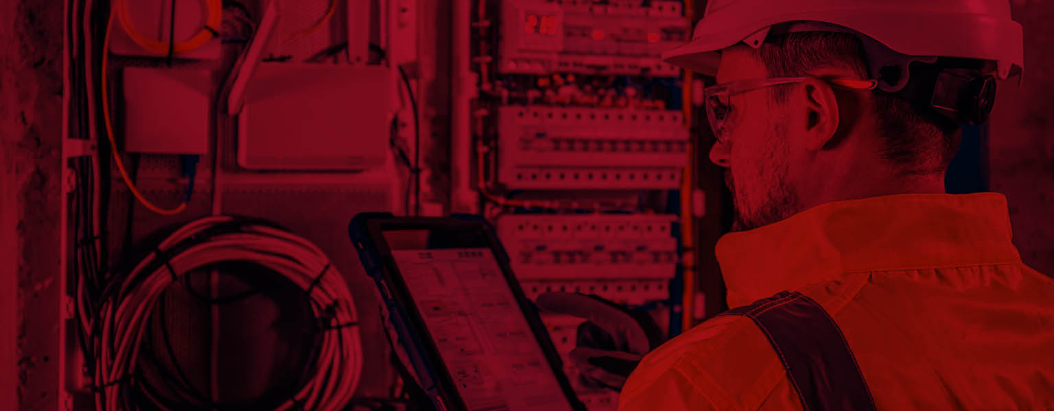 An engineer in a hi-vis jacket inspecting a control panel with a tablet