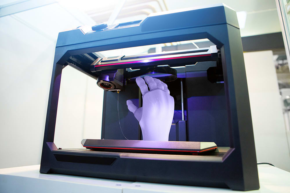 A 3D printer printing out a mechanical hand for prosthetic use in healthcare, highlighting new technology trends in the medical field.