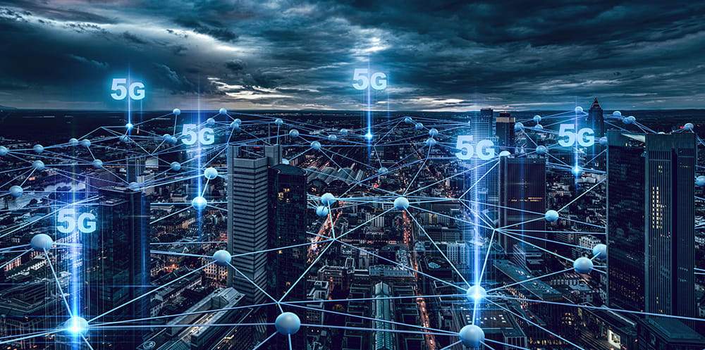 An overlooking shot of a city at night, with 5g icons above skyscrapers and blue digital connecting lines between buildings, to symbolise 5g connectivity within businesses.