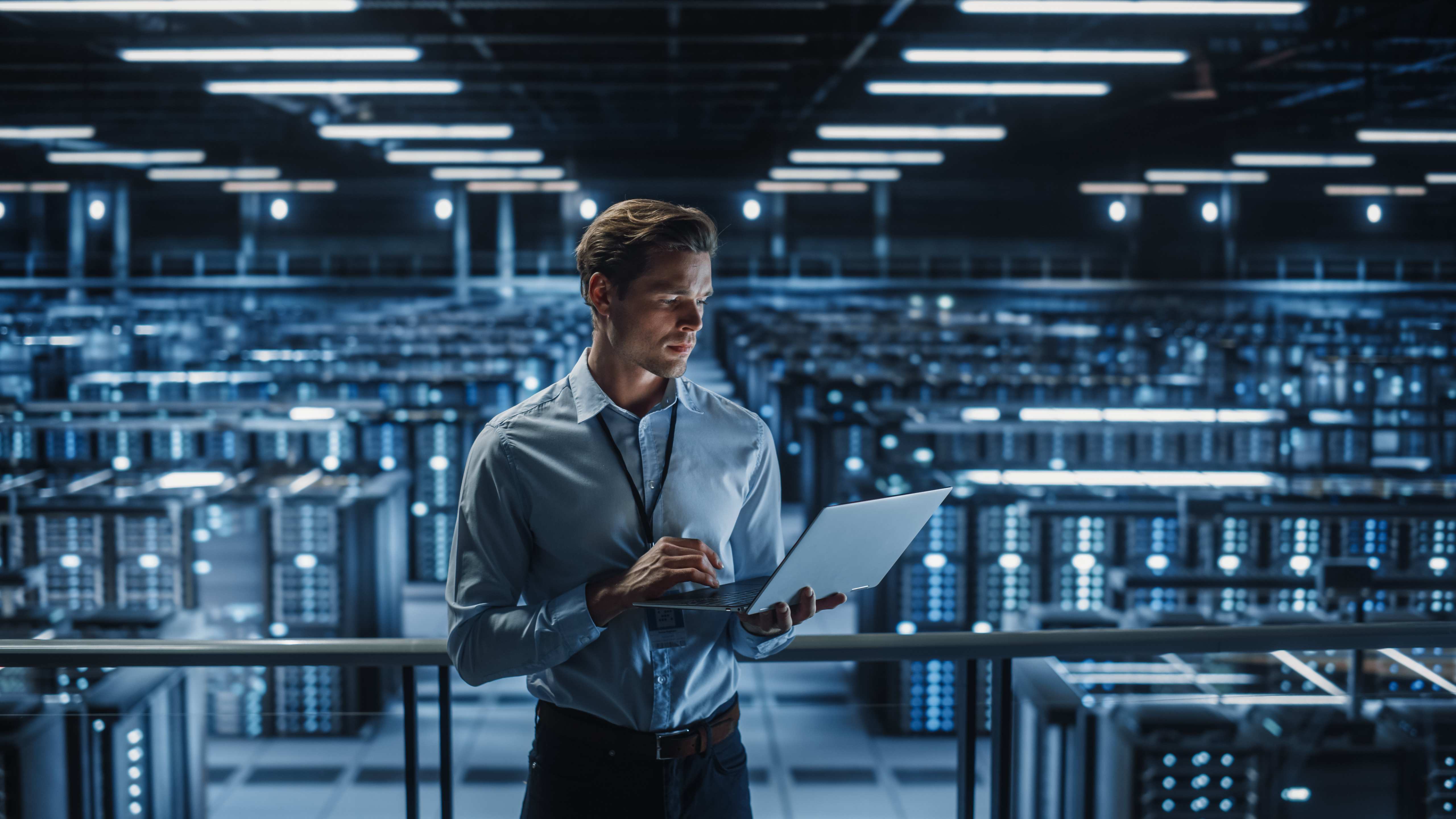 A man in a blue shirt holding a laptop, inside a quantum data center.