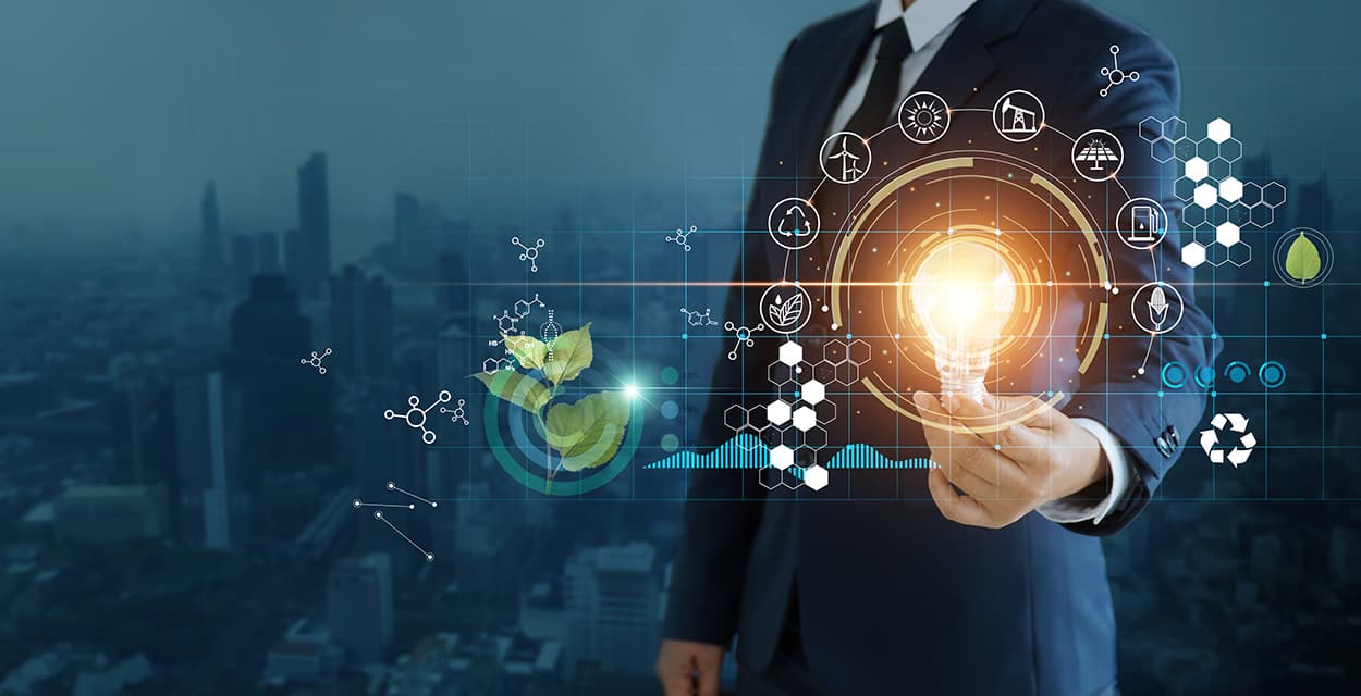 A person in a suit holds a glowing lightbulb with digital icons representing energy, sustainability, and technology.