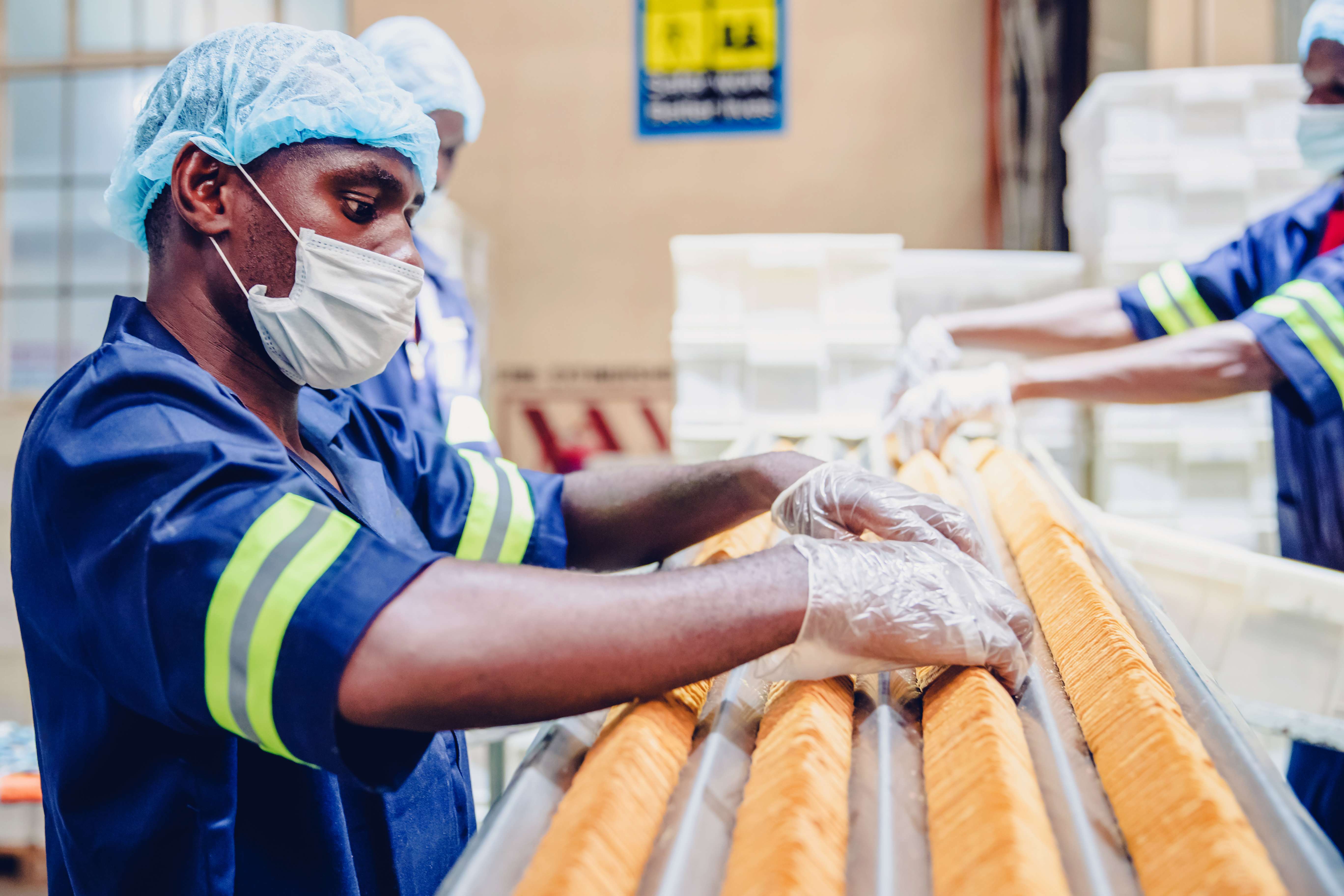 A worker in a dark blue shirt wearing a face mask and hair net, sorting through food for cross-contamination in a food production factory.