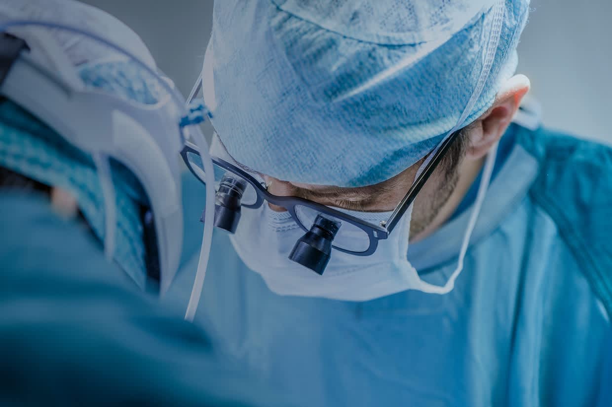 A surgeon operating, wearing glasses attached with accessories to enhance his vision.