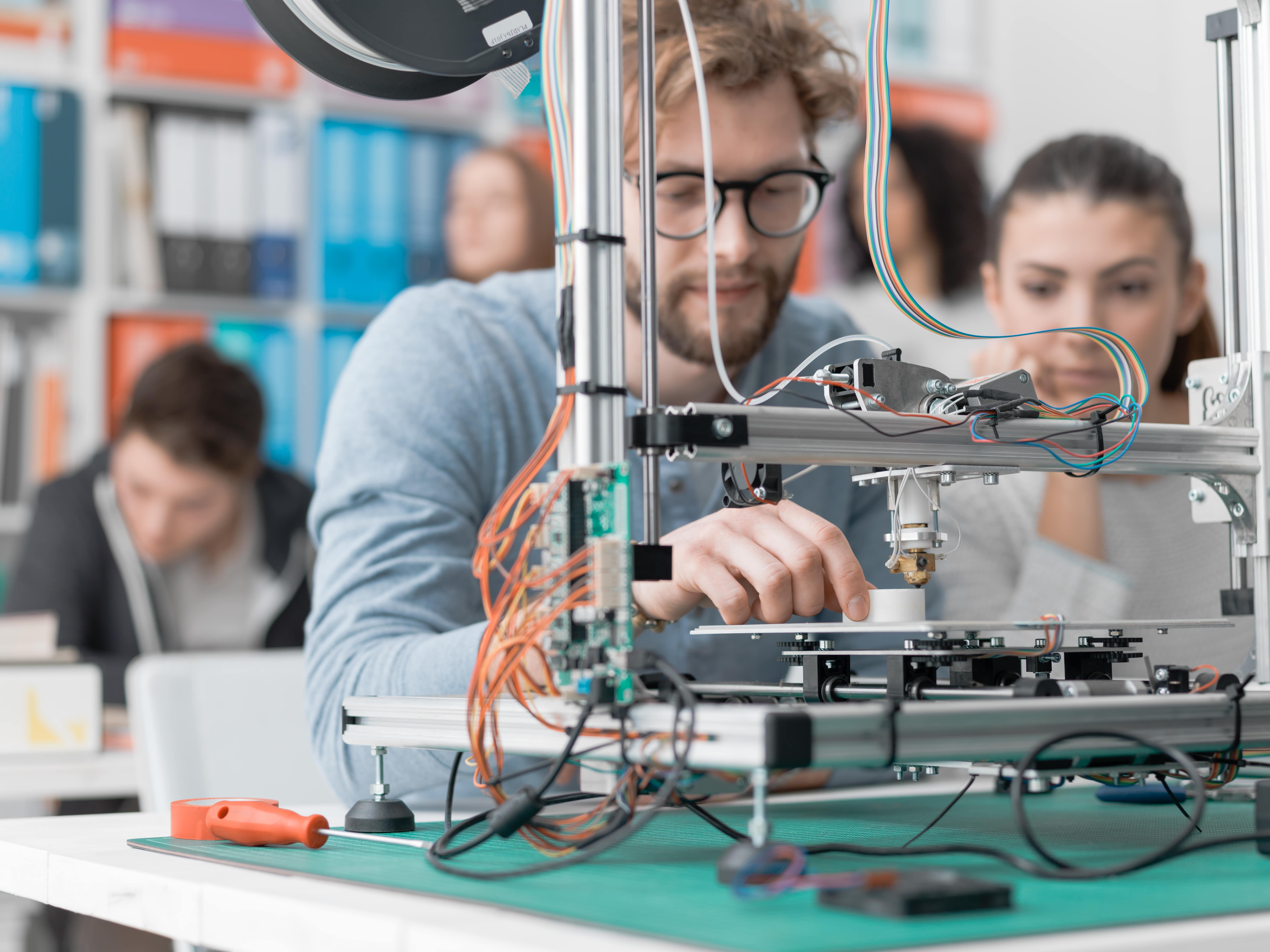 Students operating a 3D printer in a lab environment while working with food-safe printing materials and components.
