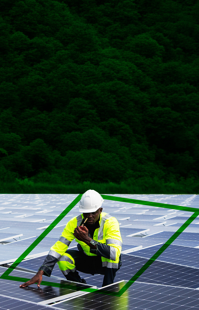 Two workers wearing hi-vis clothing and safety helmets working with electrical equipment in a large warehouse.