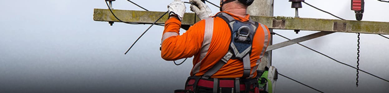 man in a hard hat working at height on top of a ladder inspecting a cable