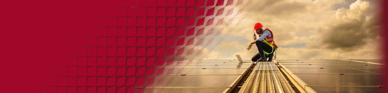 An engineer in PPE, talking on a walkie talkie and inspecting a solar panel.