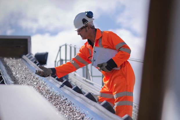 Man wearing full PPE and hard hat, inspecting aggregates