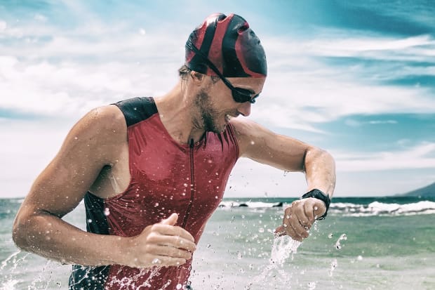 Triathlon competition swimmer exiting the ocean, looking at heart rate monitor tracker on smart watch