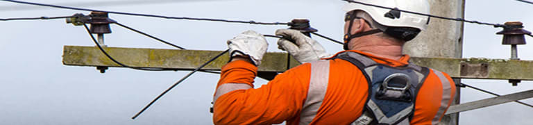 man in a hard hat working at height on top of a ladder inspecting a cable