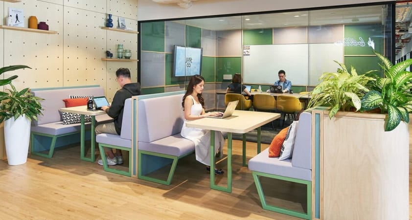 Modern coworking space with cozy booths, open seating, and vibrant greenery for a productive environment.