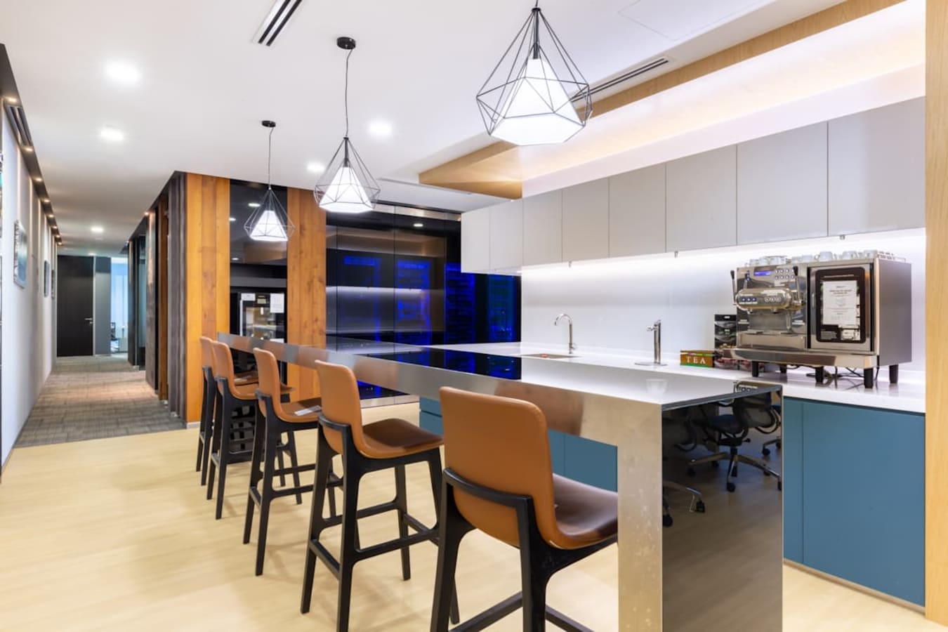 Modern coworking kitchen with sleek bar seating, stylish lighting, and coffee amenities.