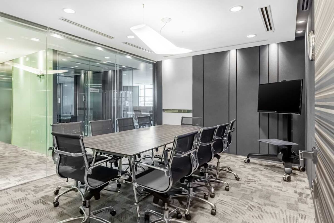 Modern conference room with sleek seating, large table, and AV setup. Glass walls enhance openness.