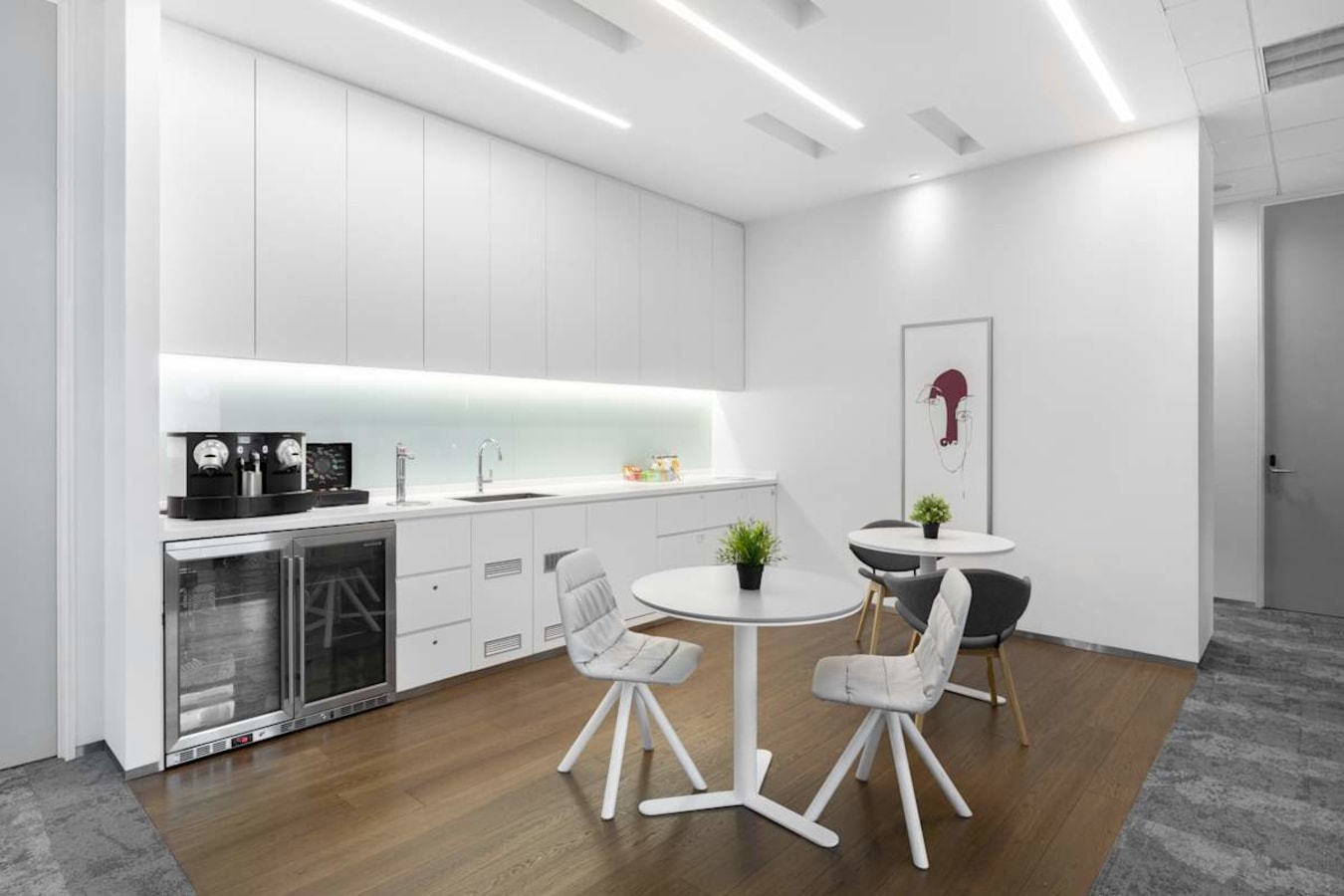 Sleek kitchenette in a modern coworking space with stylish seating and ample natural light.