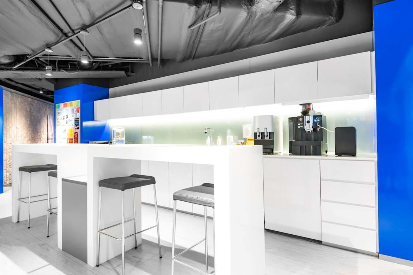 Sleek coworking kitchen with high counters, modern stools, and a convenient coffee machine.