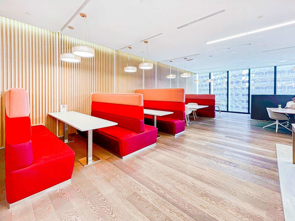 Modern coworking space with bright red booths, ample natural light, and sleek wood flooring.