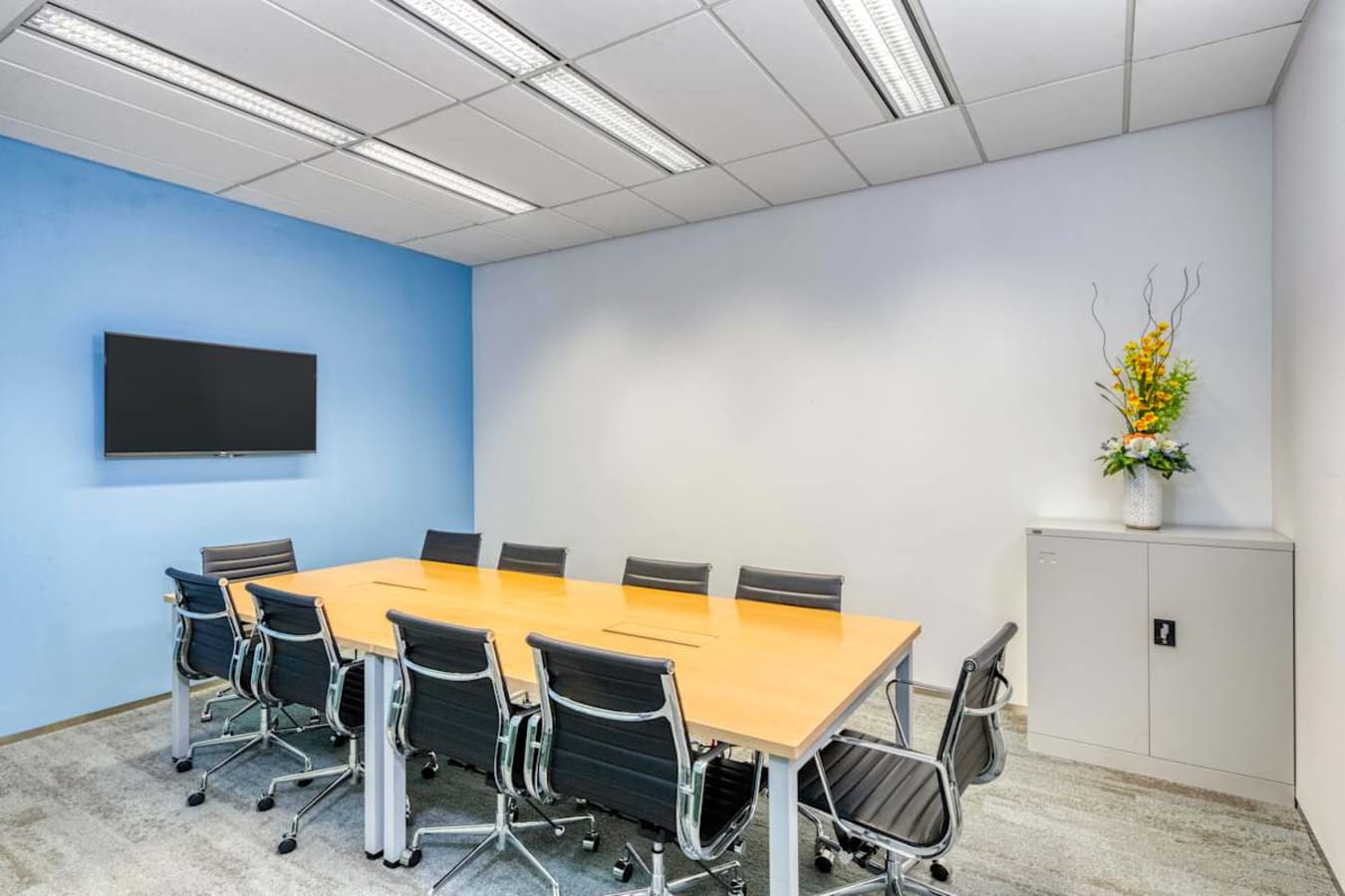 Modern meeting room with sleek chairs, vibrant accent wall, and mounted screen for presentations.