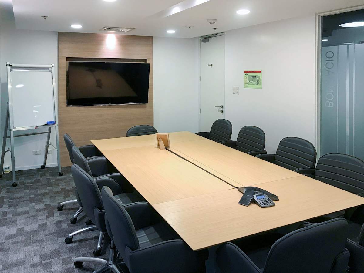 Modern meeting room with a large conference table, ergonomic chairs, and digital presentation screen.