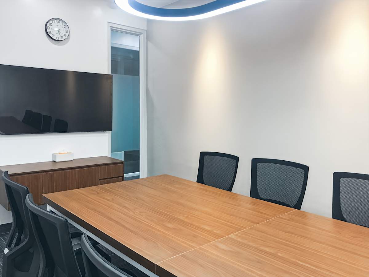 Modern meeting room with sleek wood table, ergonomic chairs, and a wall-mounted screen.