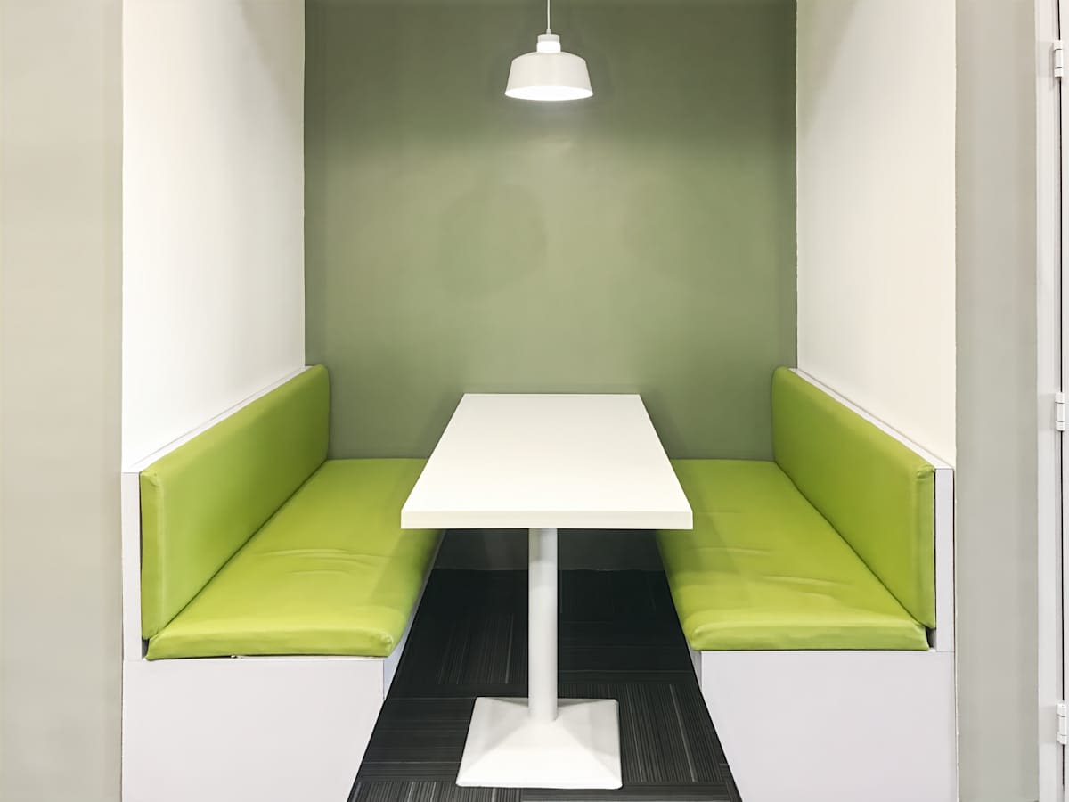 Modern booth seating with bright green cushions and a sleek white table. Cozy and inviting.