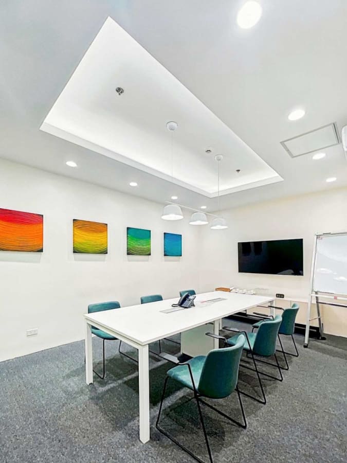 Modern meeting room with sleek white table, vibrant wall art, and ample lighting. Ideal for collaboration.