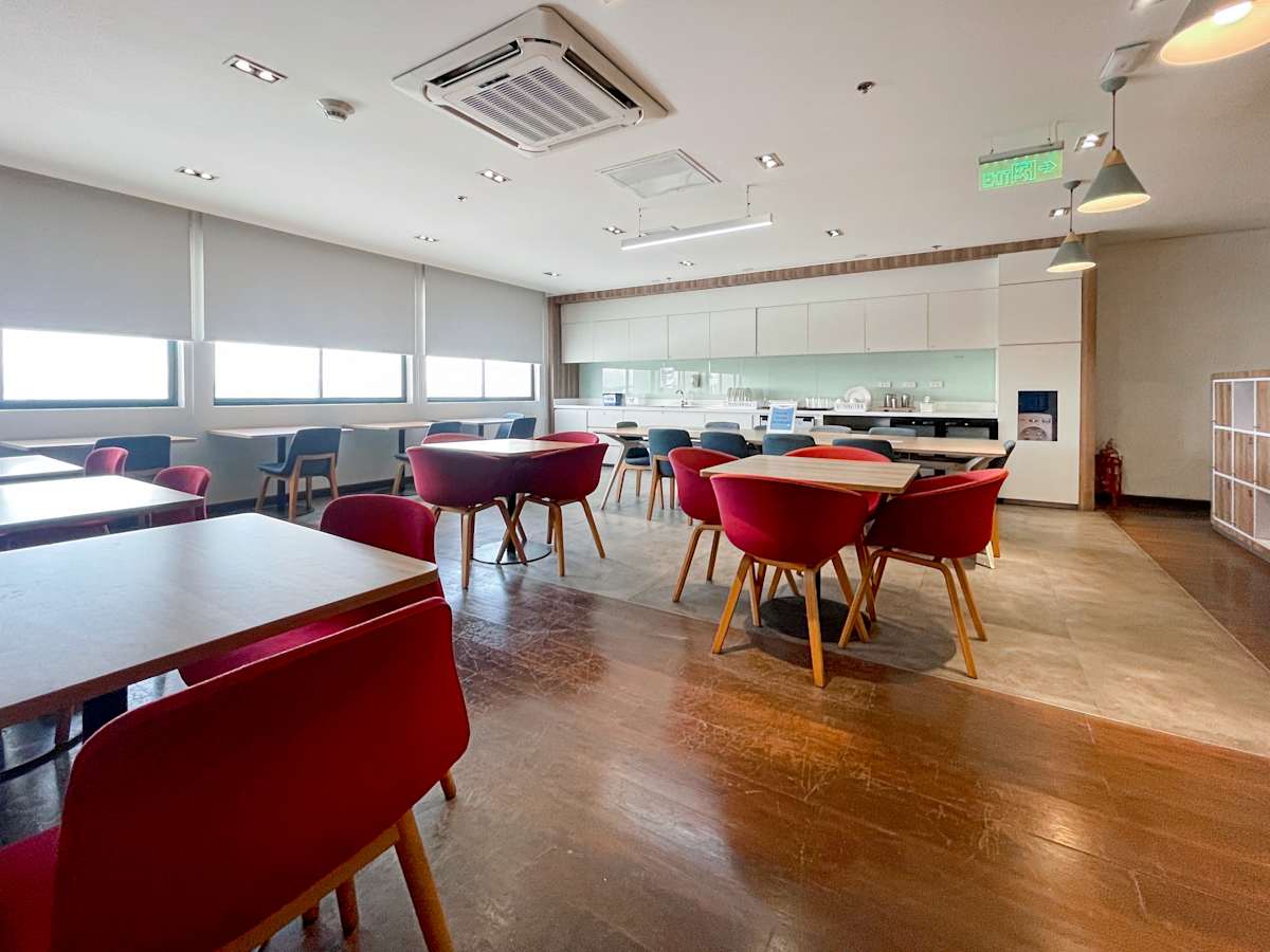 Modern coworking area with bright lighting, cozy red chairs, and a sleek kitchenette.
