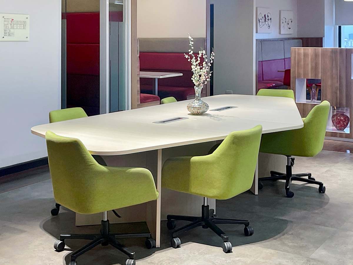 Modern coworking space featuring a sleek conference table, vibrant green chairs, and bright decor.