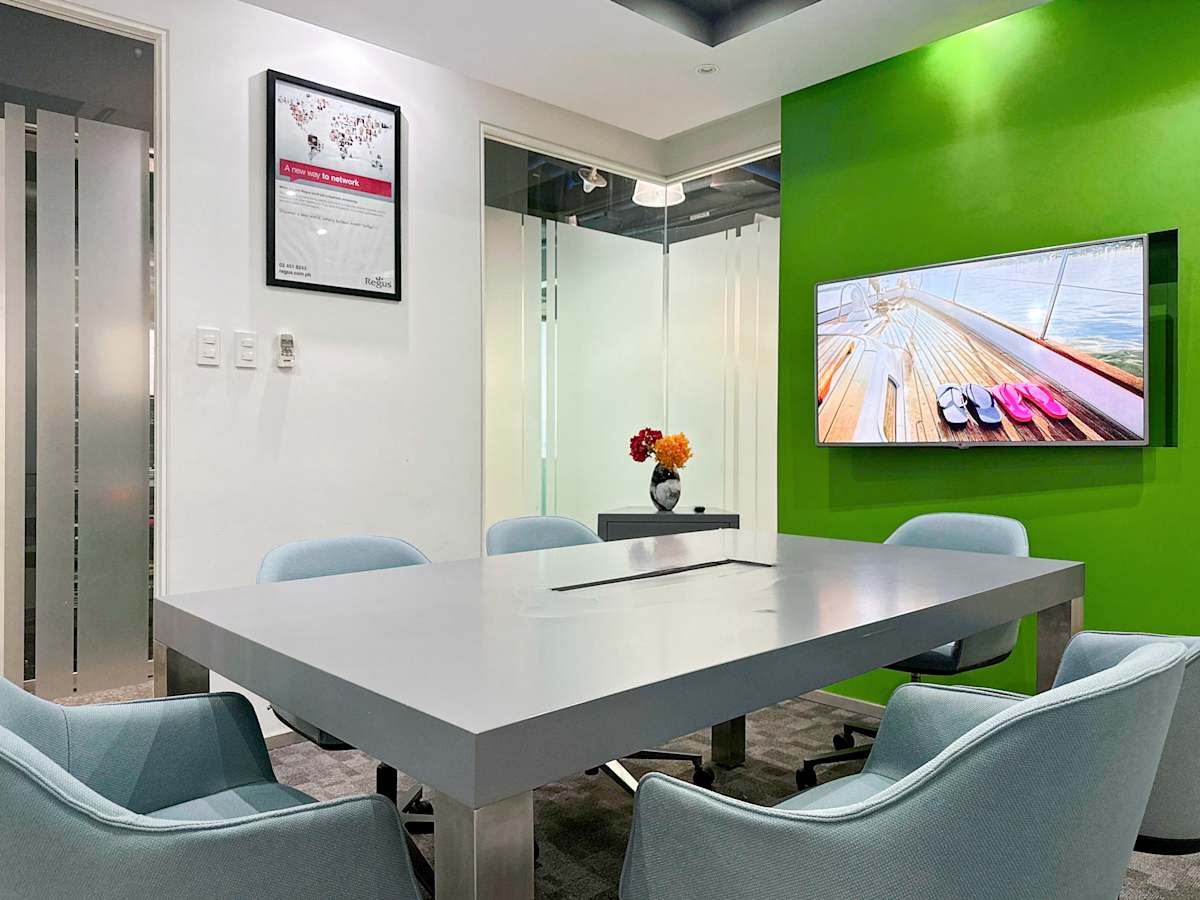 Modern meeting room with sleek table, comfy chairs, and vibrant green accent wall with TV.