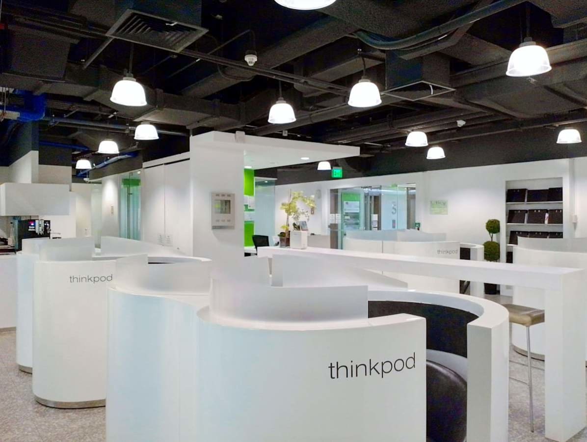 Modern coworking space featuring sleek, private pods and open seating, enhanced by bright lighting.