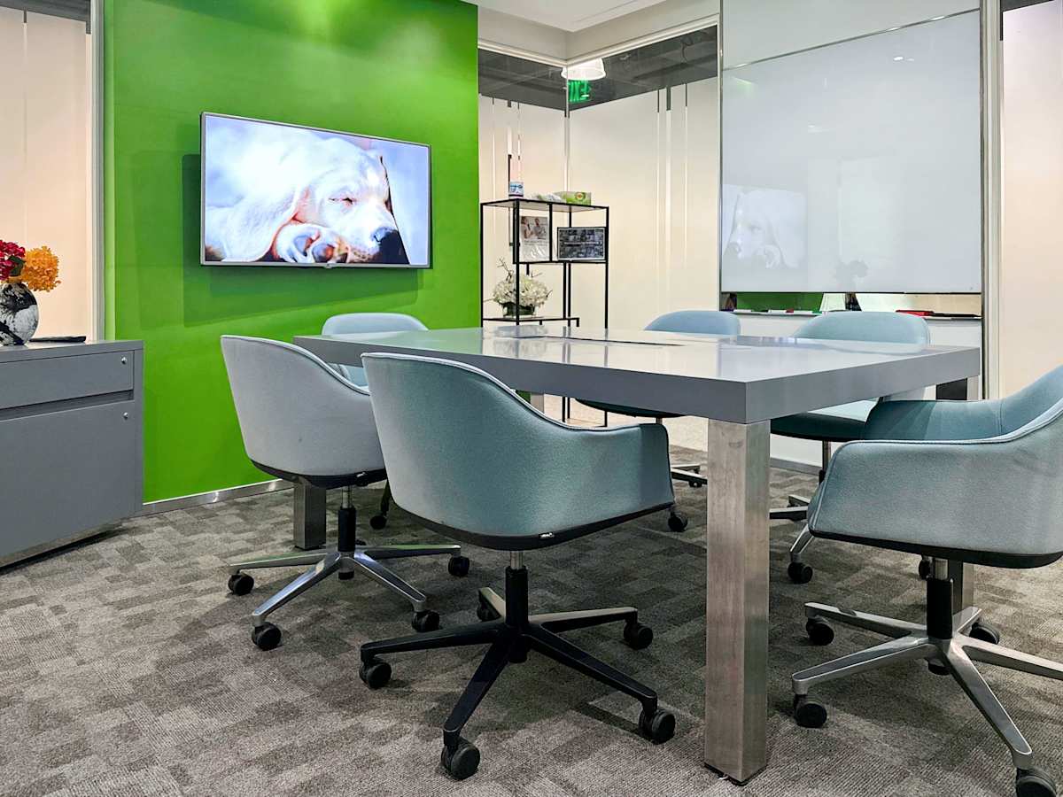 Modern meeting area with vibrant green accent wall, cozy seating, and digital display.