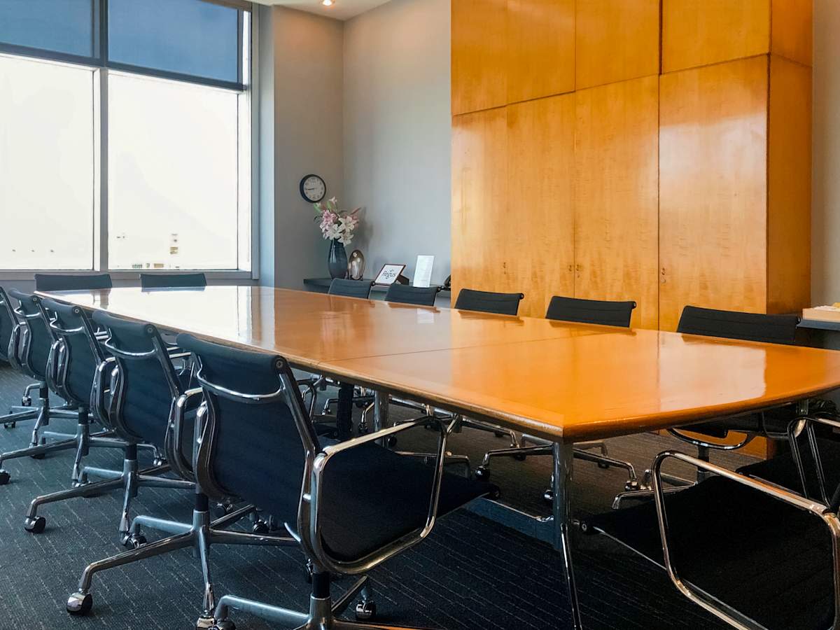 Spacious conference room with large wooden table, ergonomic chairs, and ample natural light.