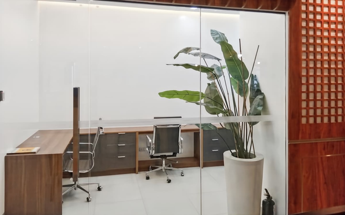 Sleek private office with glass walls, modern desk, and vibrant greenery. Ideal for focused work.