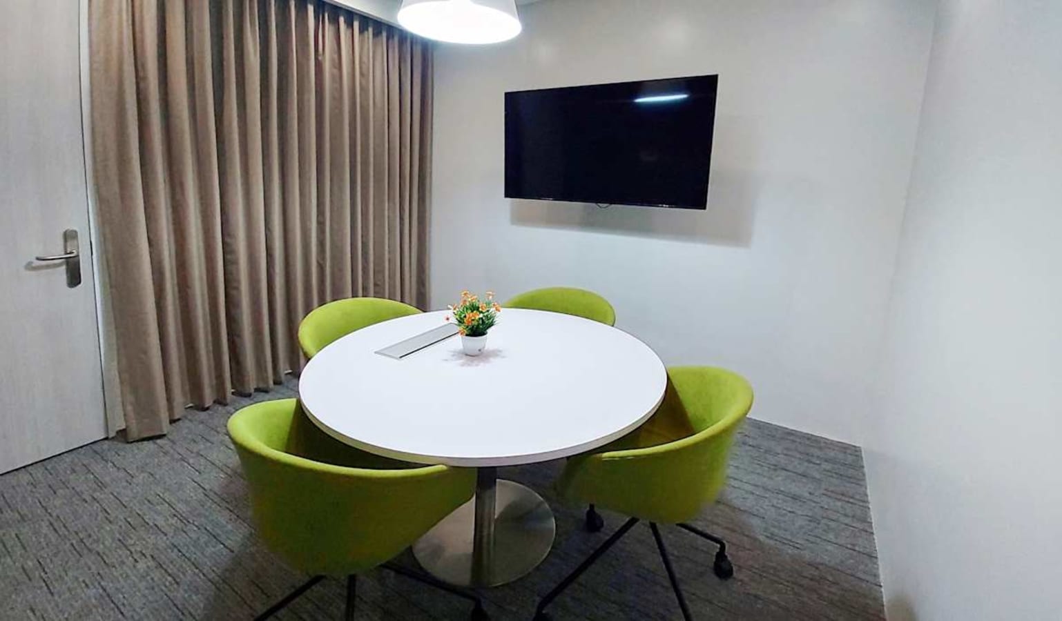 Modern meeting room with a round table, green chairs, and wall-mounted TV for presentations.