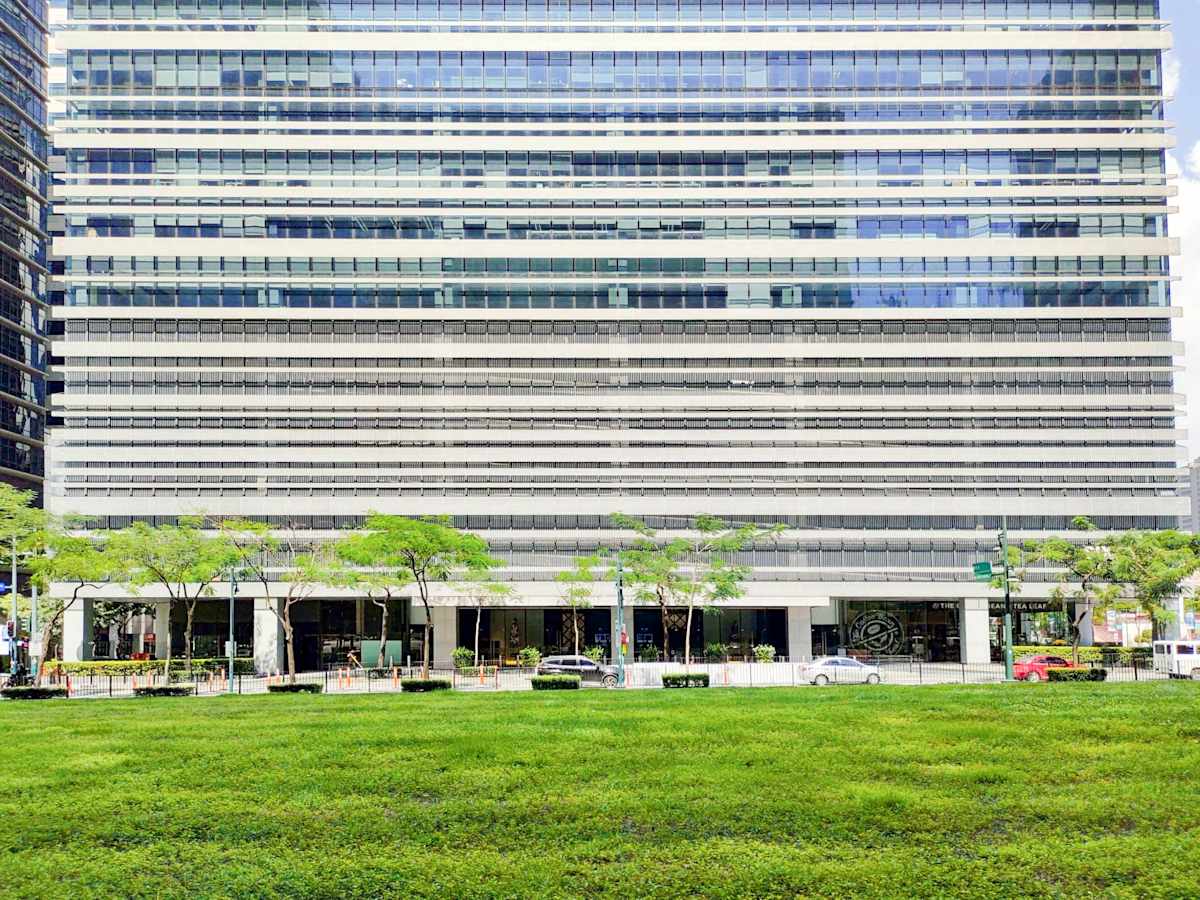 Modern office building with expansive glass facade and a vibrant green space in front.