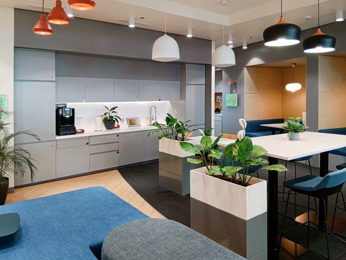 Modern coworking space with ample seating, plants, and a kitchenette, ideal for collaboration.