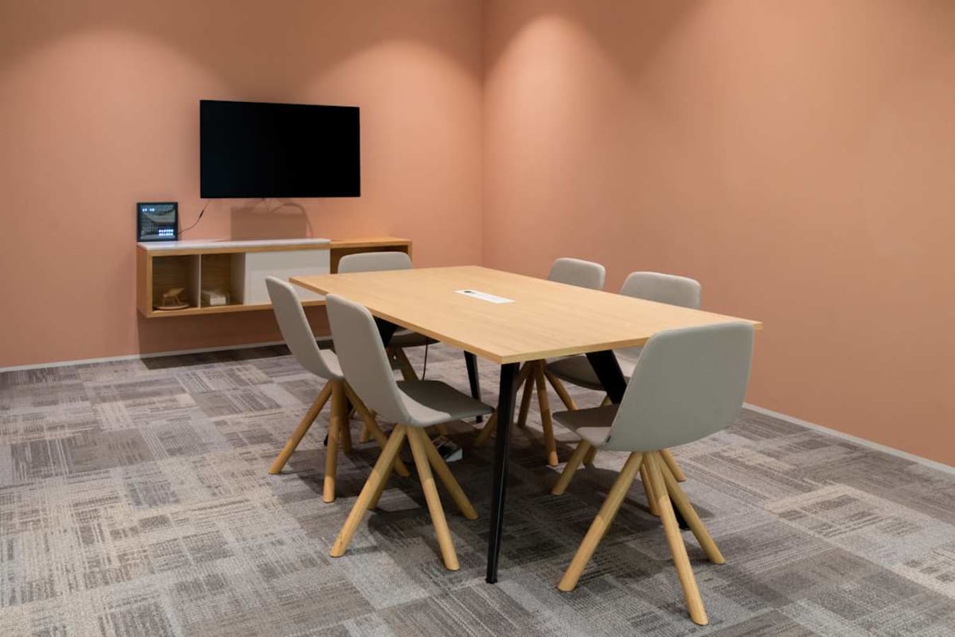 Modern meeting room with seating for six, a wall-mounted screen, and contemporary furnishings.