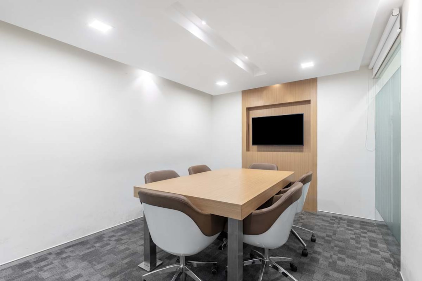 Modern meeting room with sleek chairs, minimalist décor, and a wall-mounted screen.