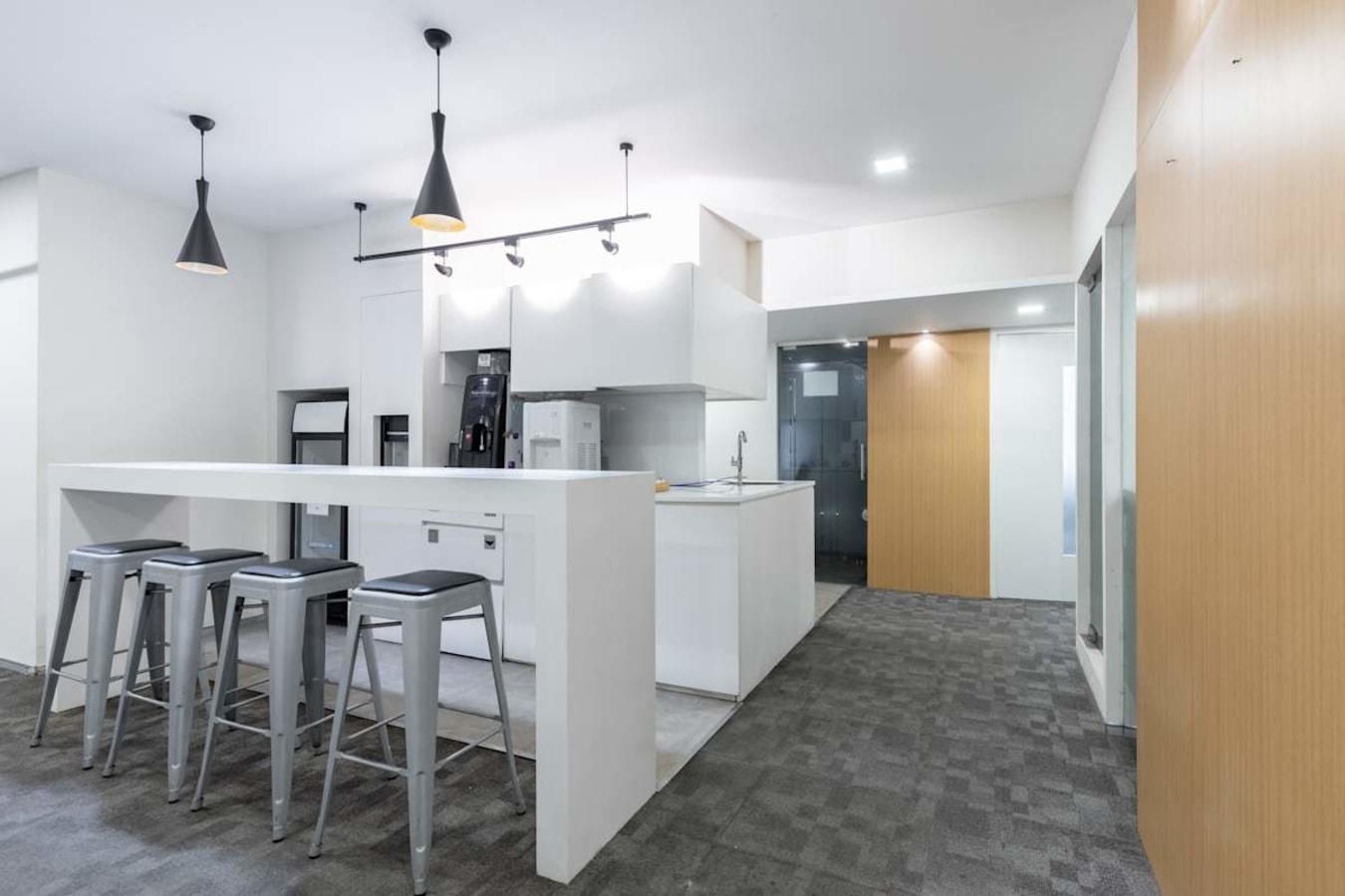 Modern coworking kitchen area with sleek counters, bar seating, and bright lighting.