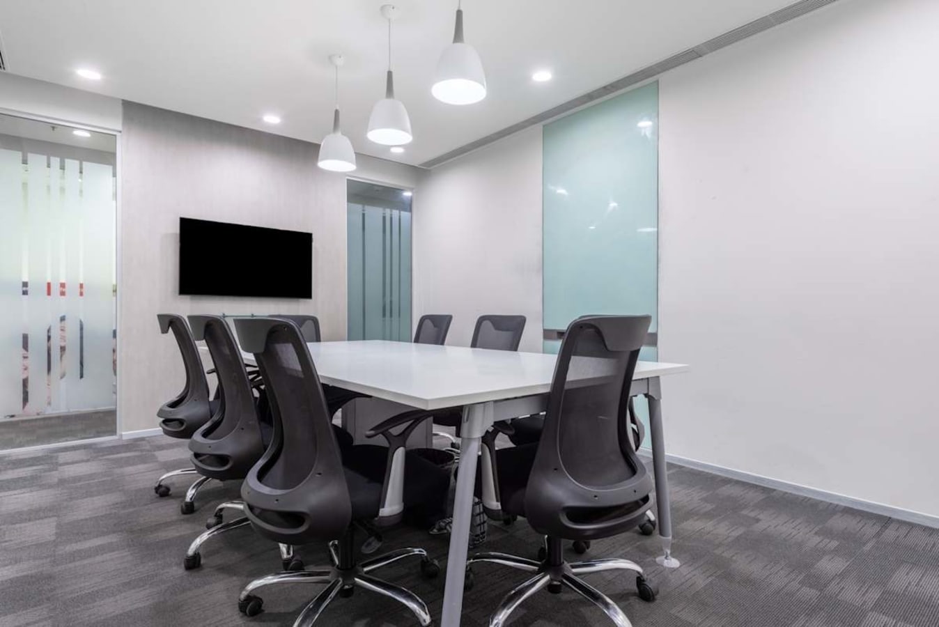 Modern meeting room with sleek chairs, ample lighting, and a wall-mounted screen in a coworking space.